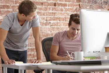 Young men talking at desk with computer - CUF42903