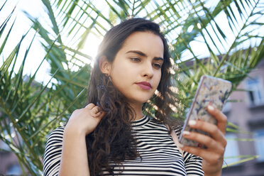 Young woman using cell phone in front of a plant - ABIF00681