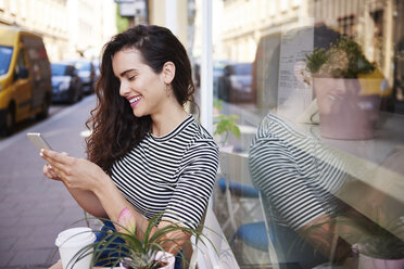 Happy young woman using cell phone at outdoor cafe in the city - ABIF00685