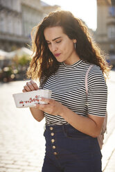 Smiling young woman eating strawberries in the city - ABIF00688