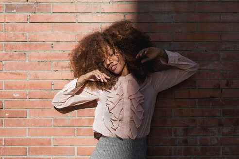 Porträt einer schönen jungen Frau mit Afrofrisur an einer Backsteinmauer im Sonnenschein - MAUF01494