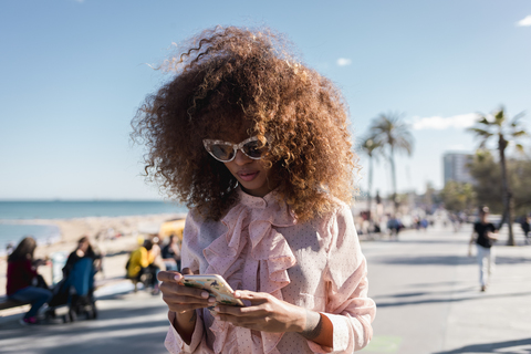 Stilvolle junge Frau, die an der Strandpromenade ein Handy benutzt, lizenzfreies Stockfoto