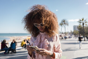 Stilvolle junge Frau, die an der Strandpromenade ein Handy benutzt - MAUF01508