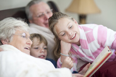 Grandparents and grandchildren reading storybook in bed - CUF42937