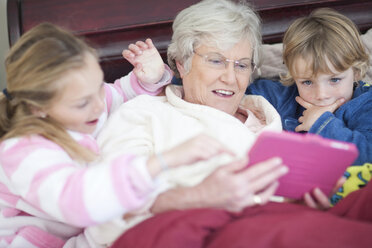 Großmutter und Enkelkinder spielen ein digitales Spiel im Bett - CUF42938