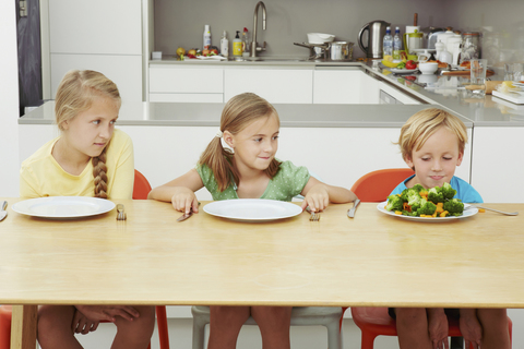 Kinder starren auf einen vollen Teller mit Grünzeug, lizenzfreies Stockfoto