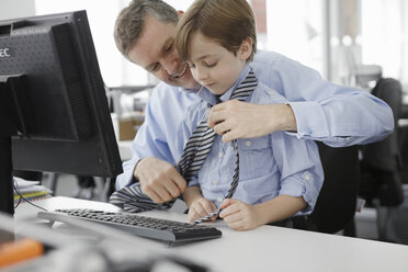 Vater legt seinem Sohn am Schreibtisch eine Krawatte an - CUF42995