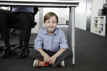 Junge sitzt auf dem Boden mit einem Geschäftsmann, der am Schreibtisch arbeitet - CUF42998