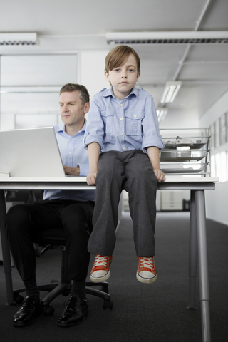 Boy sitting on desk with businessman working stock photo