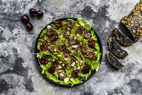 Feldsalat mit Kirschen, Feta-Käse, geröstetem Sesam und schwarzem Sepiadinkelbrot, lizenzfreies Stockfoto