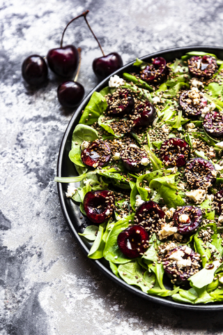 Feldsalat mit Kirschen, Feta-Käse, geröstetem Sesam und schwarzem Sepiadinkelbrot, lizenzfreies Stockfoto