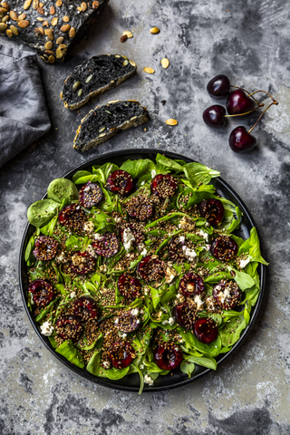 Feldsalat mit Kirschen, Feta-Käse, geröstetem Sesam und schwarzem Sepiadinkelbrot, lizenzfreies Stockfoto