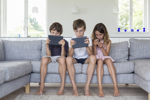 Brüder und Schwester auf dem Sofa mit digitalen Tablets und Handy, lizenzfreies Stockfoto
