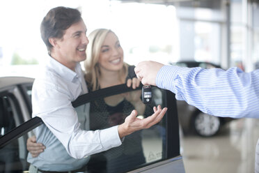 Autoverkäufer übergibt Schlüssel an Paar im Ausstellungsraum - CUF43248