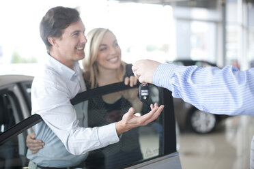 Car salesman handing key to couple in showroom - CUF43248