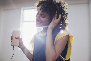 Smiling, carefree young woman listening to music with headphones and mp3 player - HOXF03645