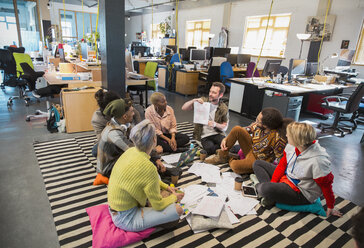 Kreative Geschäftsleute treffen sich zum Brainstorming im Kreis auf dem Boden eines Büros - CAIF20994