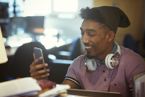 Lächelnder kreativer Geschäftsmann, der mit seinem Smartphone im Büro SMS schreibt, lizenzfreies Stockfoto