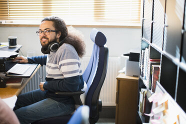 Porträt lächelnder, selbstbewusster, kreativer Geschäftsmann mit Kopfhörern bei der Arbeit im Büro - CAIF21008