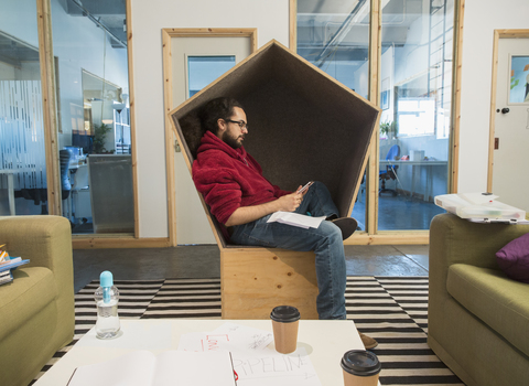 Kreativer Geschäftsmann, der sein Smartphone in einem Büroschrank benutzt, lizenzfreies Stockfoto