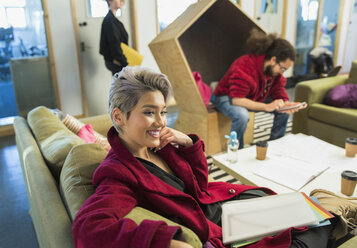 Lächelnde kreative Geschäftsfrau mit Papierkram in einem legeren Büro - CAIF21041
