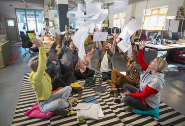 Playful, enthusiastic creative business team throwing paperwork overhead in open plan office - CAIF21043