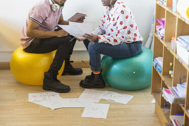 Kreative Geschäftsleute treffen sich und besprechen Papierkram auf Fitnessbällen im Büro - CAIF21049