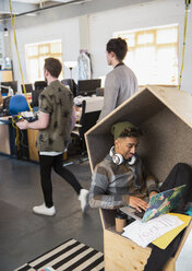Kreativer Geschäftsmann mit Kopfhörern, der einen Laptop in einem Büroraum benutzt - CAIF21053