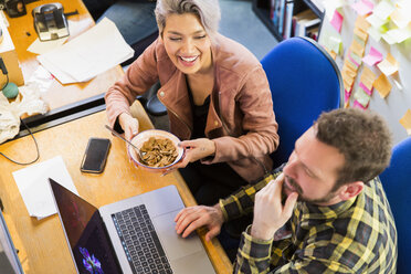 Kreative Geschäftsleute essen Müsli, arbeiten am Laptop im Büro - CAIF21065