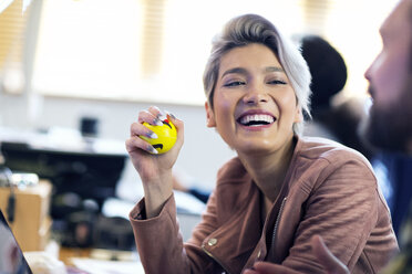 Lachende kreative Geschäftsfrau, die im Büro einen Stressball quetscht - CAIF21102