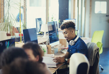 Creative businessman working at computer in open plan office - CAIF21106