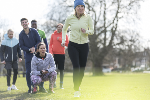 Team cheering woman running in park stock photo