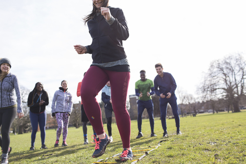 Team jubelnde Frau beim Speed Ladder Drill im sonnigen Park, lizenzfreies Stockfoto