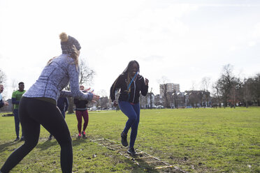 Woman cheering friend doing speed ladder drill in sunny park - CAIF21159