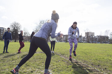 Frau jubelt Klassenkameradin beim Speed Ladder Drill im sonnigen Park zu - CAIF21164