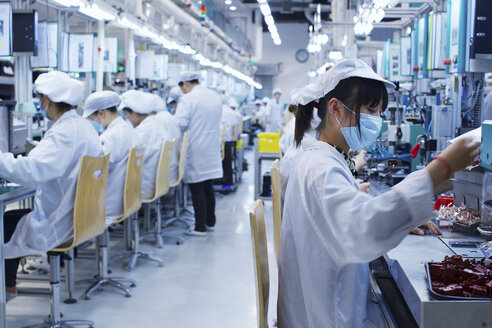 Gruppe von Arbeitern in einer Fabrik für Kleinteile in China, die Schutzkleidung, Hüte und Masken tragen - CUF43439