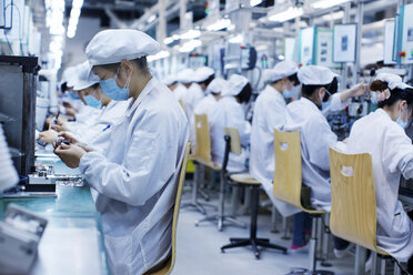 Gruppe von Arbeitern in einer Fabrik für Kleinteile in China, die Schutzkleidung, Hüte und Masken tragen - CUF43440