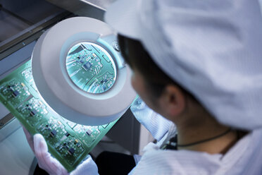 Worker at small parts manufacturing factory in China looking through magnifier at microchips - CUF43442