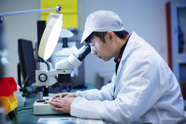 Workers at small parts manufacturing factory in China looking through microscope - CUF43444