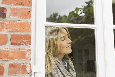 Mid adult woman by window with eyes closed, smiling - CUF43485