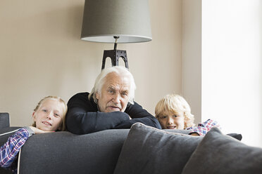 Porträt von Großvater und Enkelkindern, die sich an ein Sofa lehnen - CUF43493