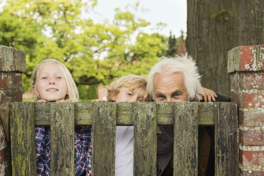Großvater und Enkelkinder blicken über das Holztor - CUF43504