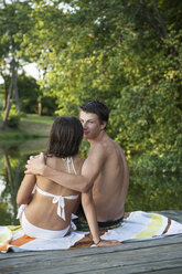 Ein junges Paar, ein Junge und ein Mädchen, sitzen dicht beieinander auf einem Holzsteg an einem Wasserbecken. - MINF00042