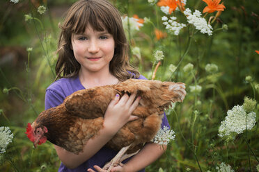 A young girl holding a domestic hen, with brown feathers and a red comb. - MINF00048