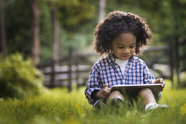 Ein kleiner Junge sitzt im Gras und benutzt einen Tablet-Computer. - MINF00074