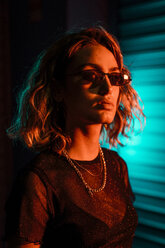 Stylische junge Frau bei Nacht vor einem Rollladen, mit Sonnenbrille - KKAF01241