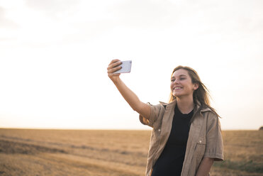 Junge Frau steht auf einem Feld und macht ein Smartphone-Selfie - ACPF00125