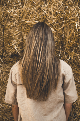 Schöne junge Frau vor Heuballen stehend, Rückansicht, lizenzfreies Stockfoto