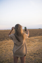 Junge Frau steht auf einem Feld und macht ein Smartphone-Selfie - ACPF00135