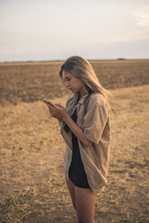 Junge Frau steht auf einem Feld und benutzt ein Smartphone - ACPF00136